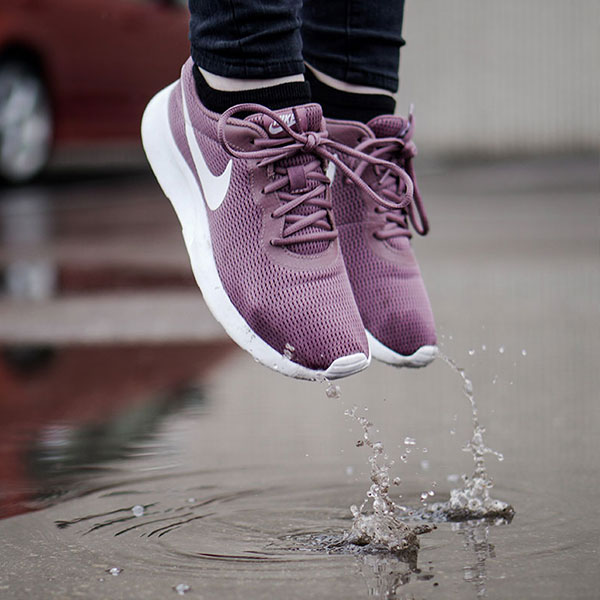 person in magenta tennis shoes jumping in a puddle